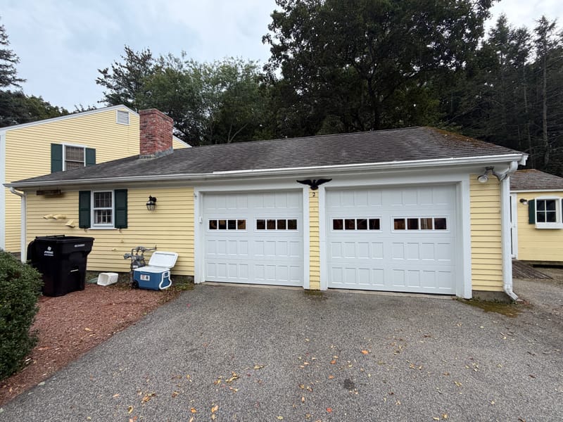 Two new white garage doors with a row of windows on a yellow Cape in Acton, MA