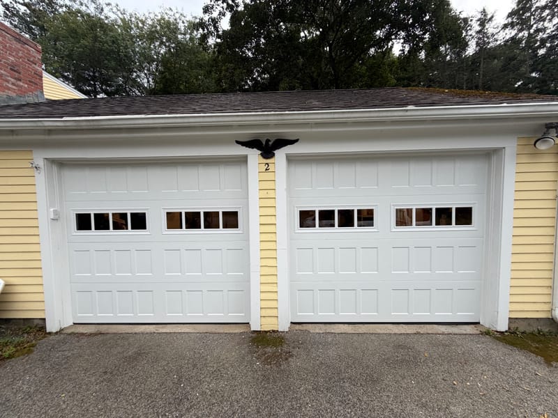 Two new white Amarr Hillcrest garage doors with a row of windows on a yellow house in Acton, MA