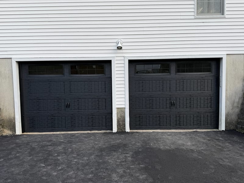 Two black carriage-style garage doors with windows under a white house