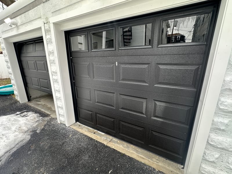 Close view of a new black raised-panel garage door with windows on a white block garage