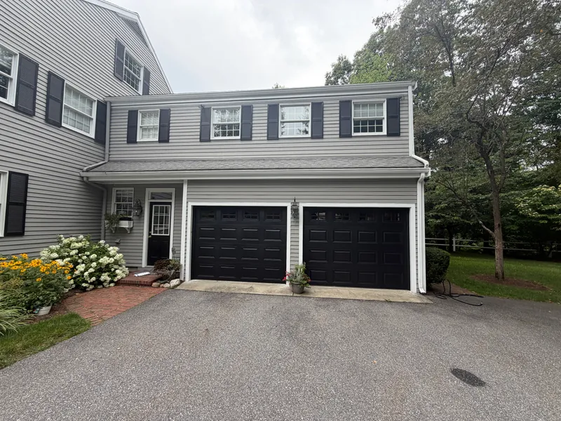 Two black raised-panel garage doors with windows on a gray colonial