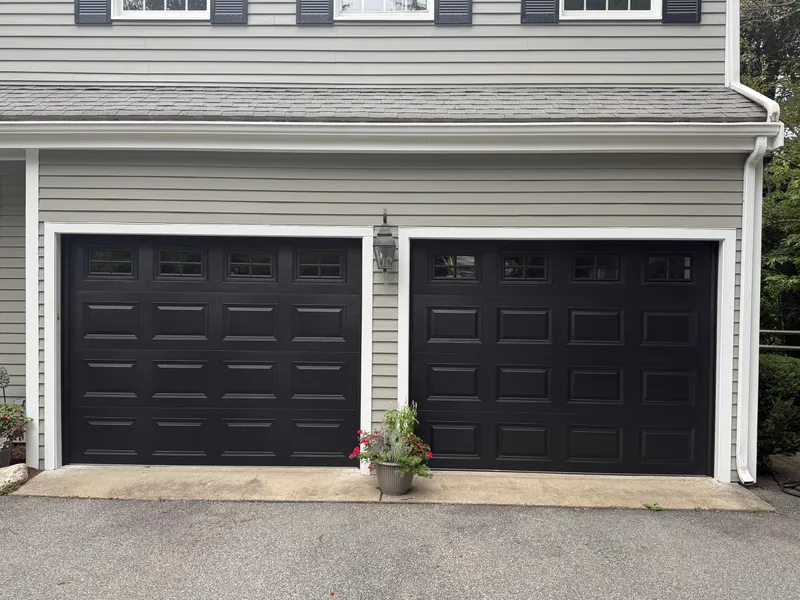 Close view of two new black raised-panel garage doors with a row of windows on a gray colonial