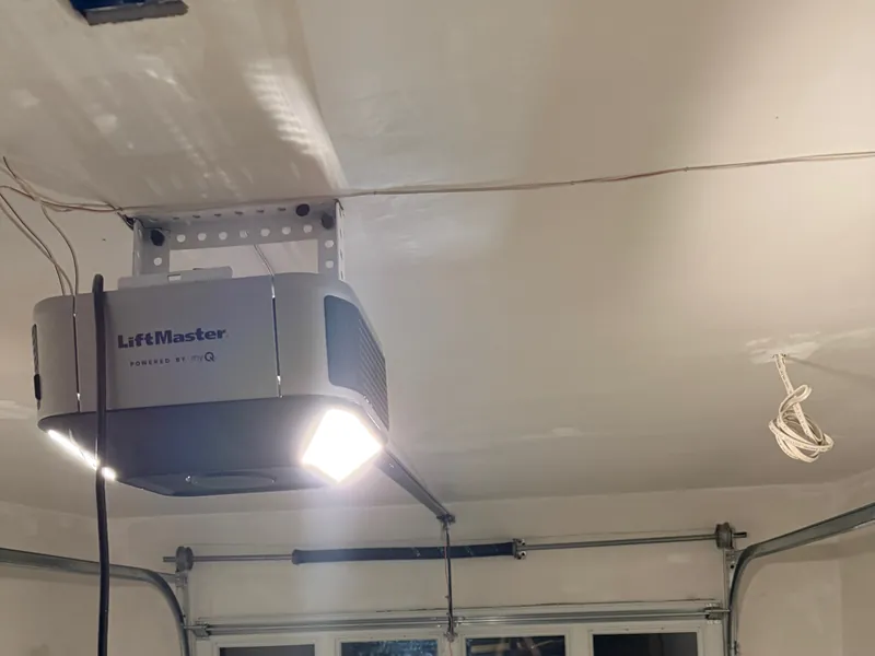 LiftMaster opener with its light on above a new white garage door with windows in a newly built garage