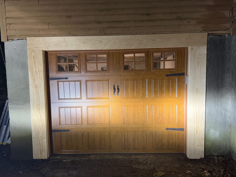 Woodgrain carriage-style garage door with a row of windows and new trim